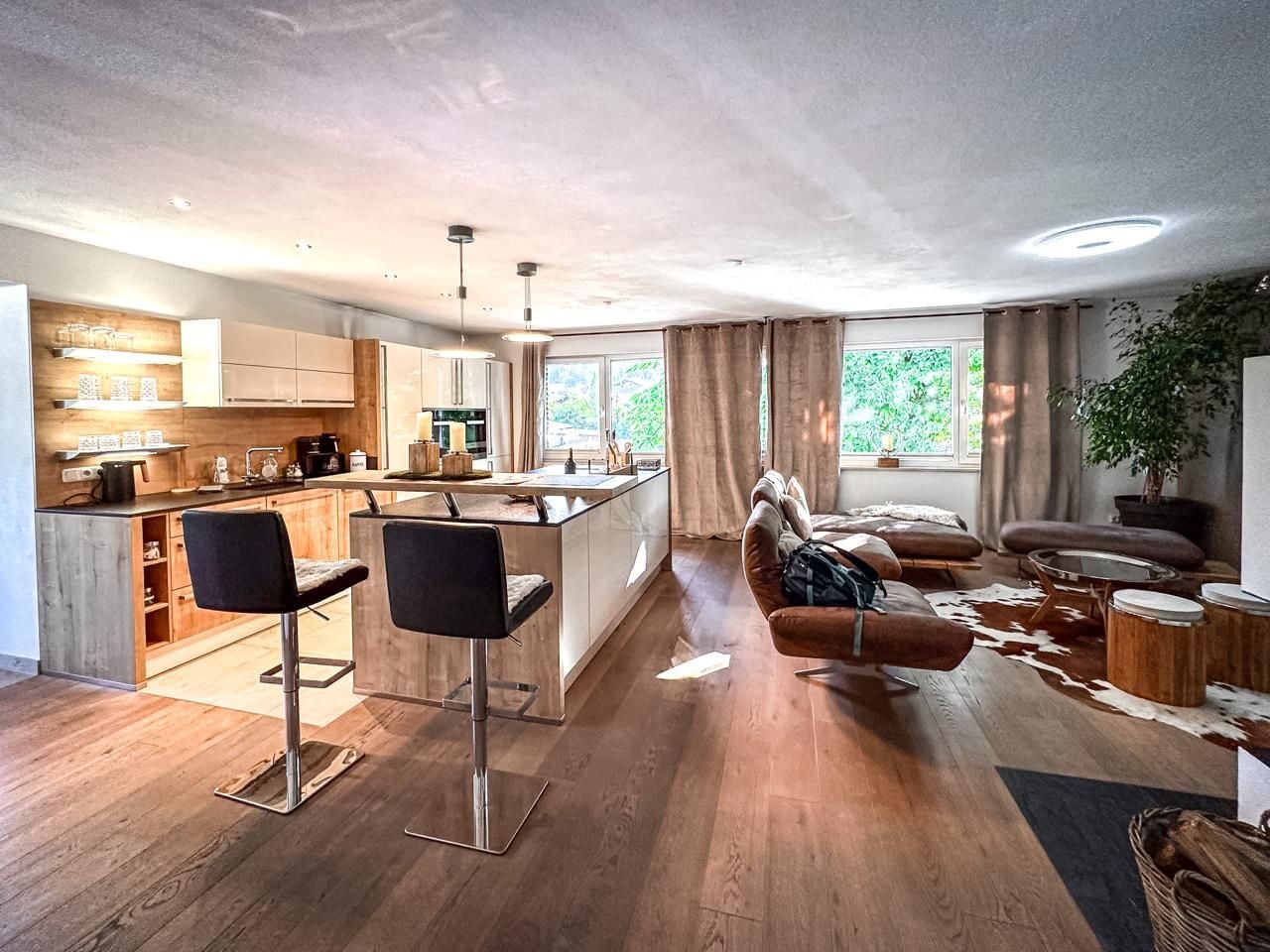 Eine moderne Küche mit einer zentralen Kochinsel, Barhocker und einem Essbereich mit Sofa und Couchtisch.