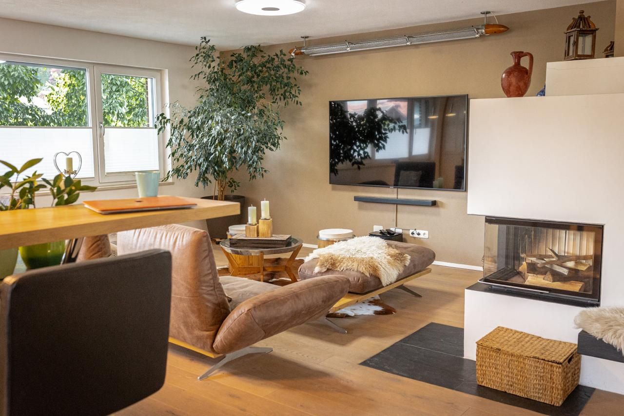 Un salon moderne avec une cheminée, un téléviseur, un coin repas et une grande plante.