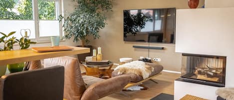 Una sala de estar moderna con chimenea, televisión, comedor y una planta grande.