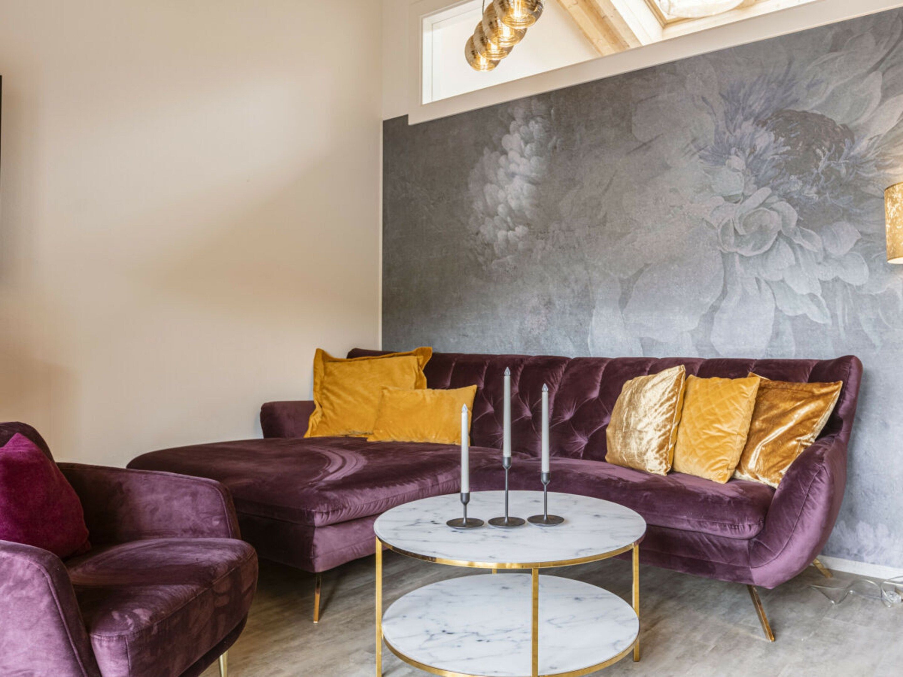A room with a purple velvet sofa, a round marble coffee table, and a wall with a floral mural.