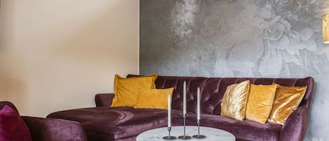 A room with a purple velvet sofa, a round marble coffee table, and a wall with a floral mural.