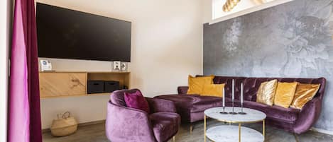 A modern living room with a large flat-screen TV, a sofa set, and a round coffee table.