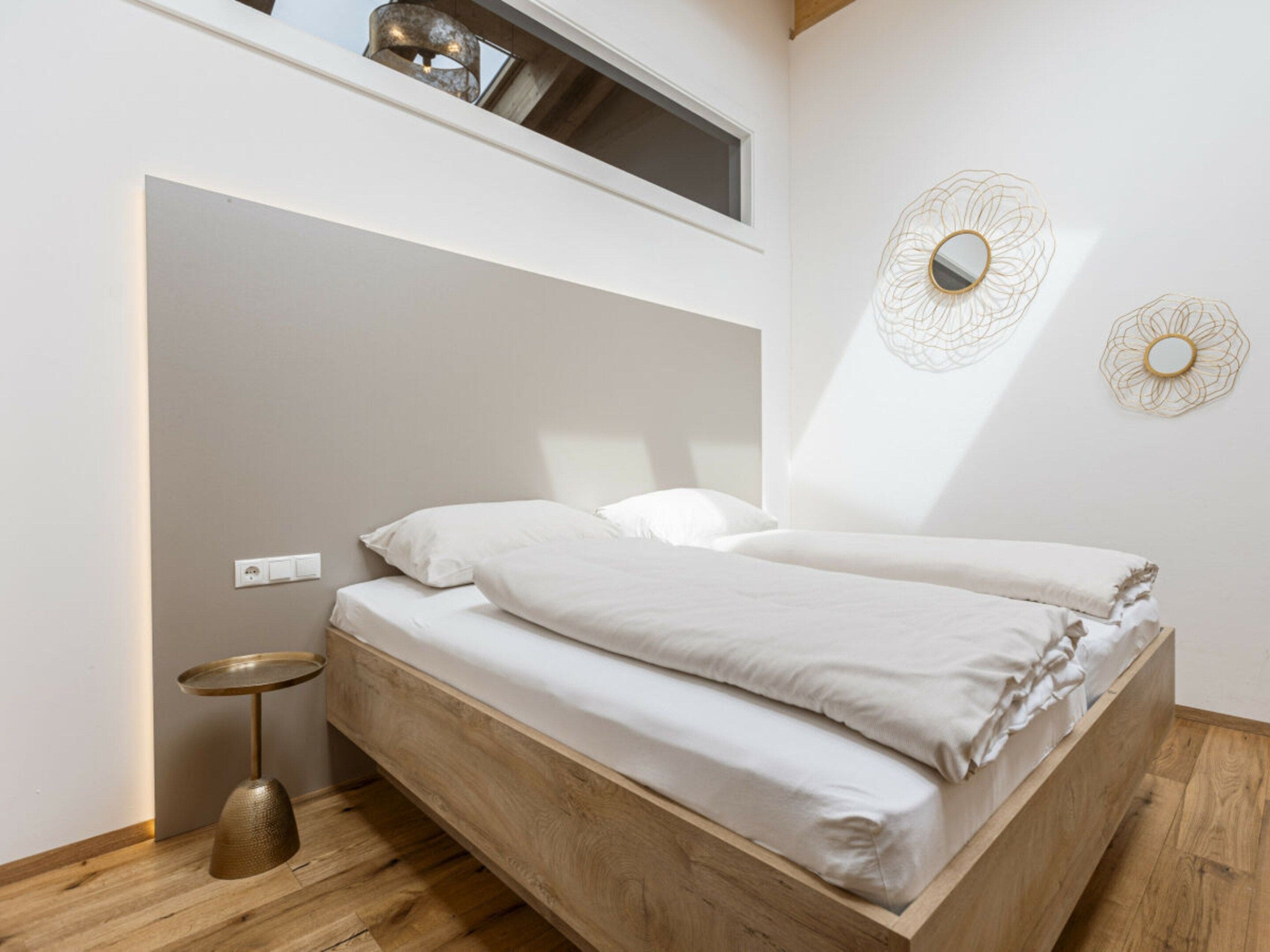 A minimalist bedroom with a bed, a small round table, and a wall-mounted light fixture.