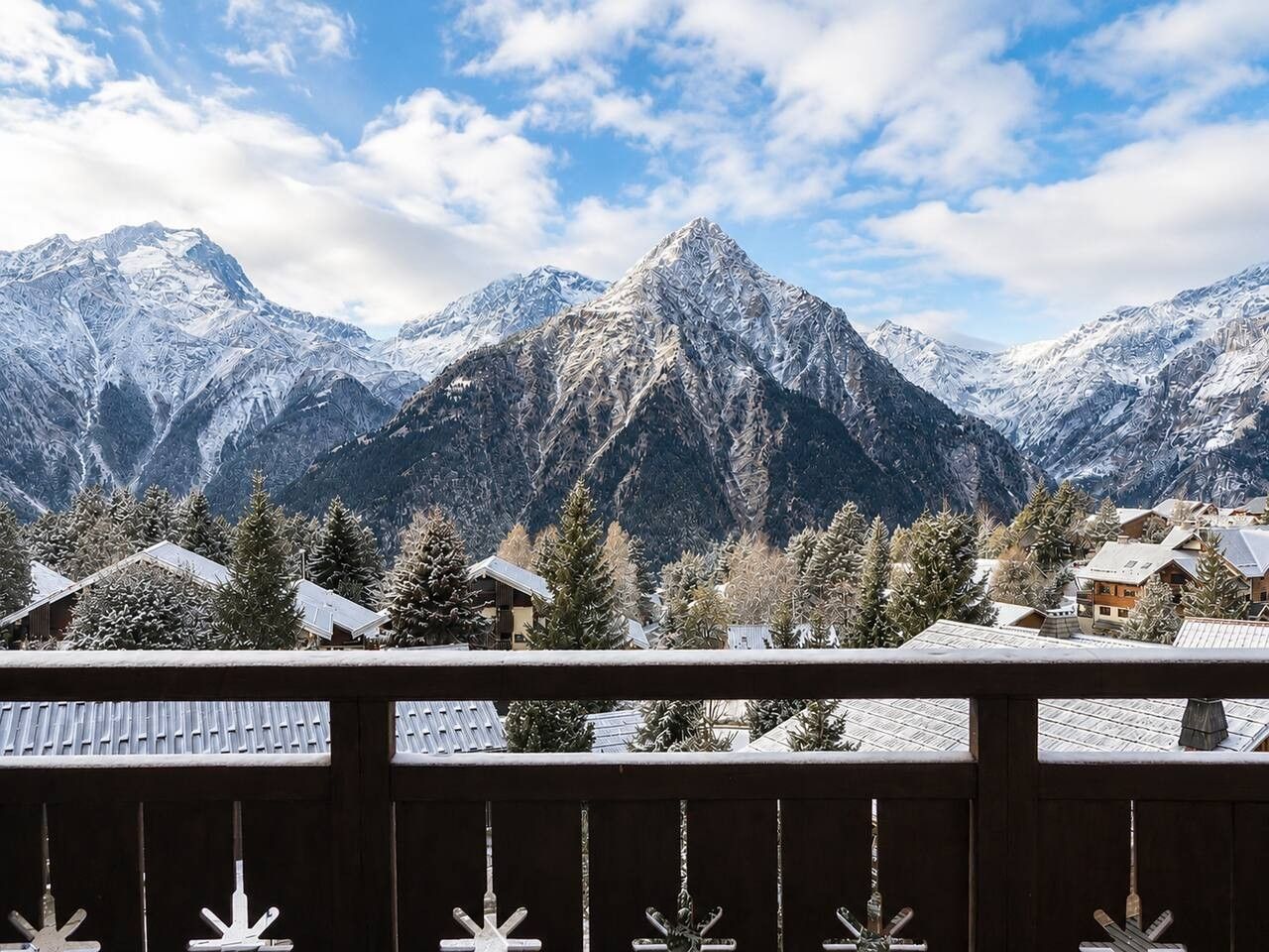Un paysage de montagne avec des sommets enneigés et une vue sur un quartier résidentiel avec des maisons et des arbres.