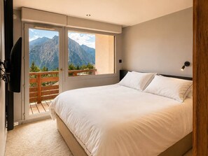 Une chambre avec un lit, une télévision et un balcon offrant une vue sur la montagne.