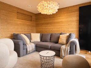Un salon moderne avec un canapé d’angle, une table basse ronde et un luminaire au plafond original.