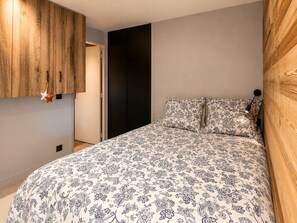 A bedroom with a large bed, wooden wardrobe, and a door leading to another room. - Dorion Lodge, Glacier View - Alto Society (Les Deux Alpes)