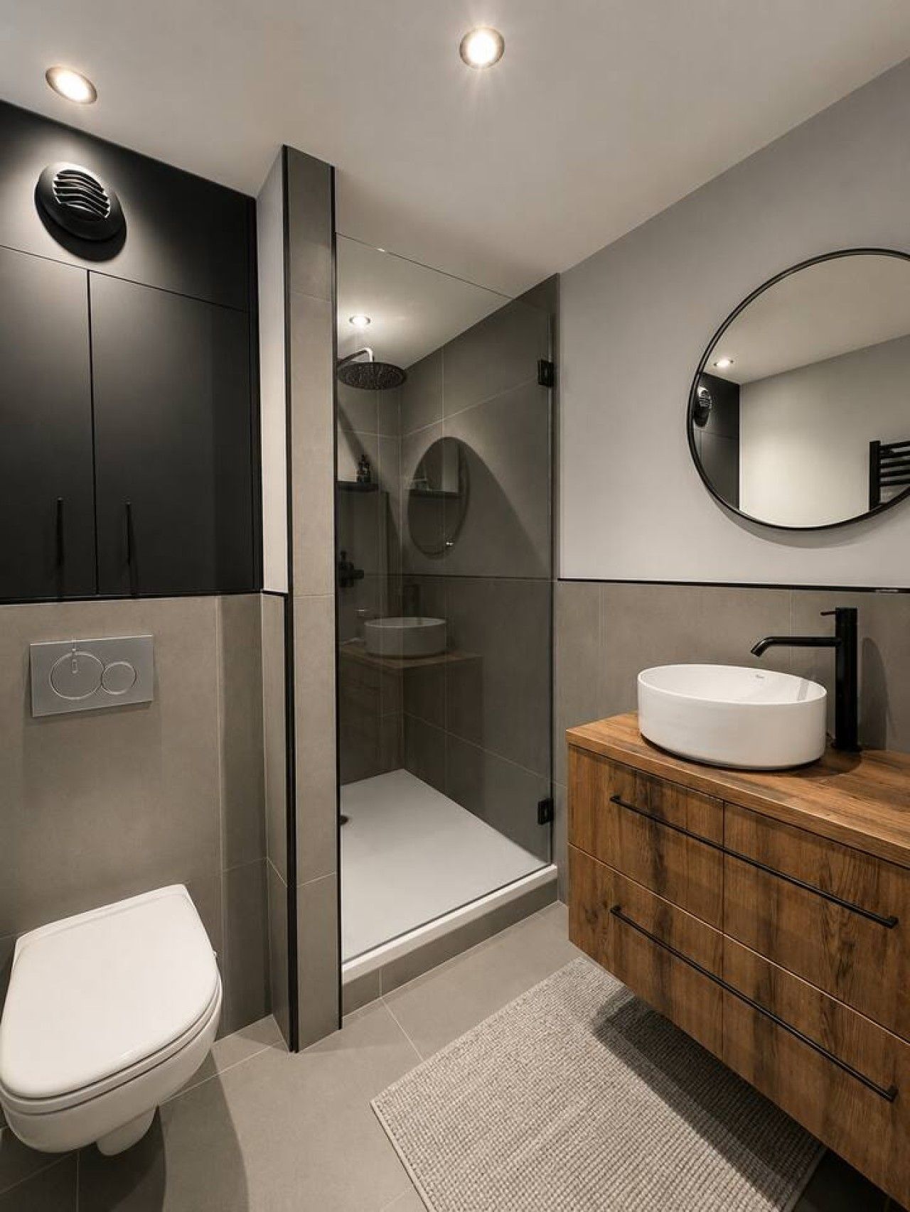 Een moderne badkamer met een douche met glazen wand, een houten wastafelmeubel, een ronde spiegel en een toilet.
