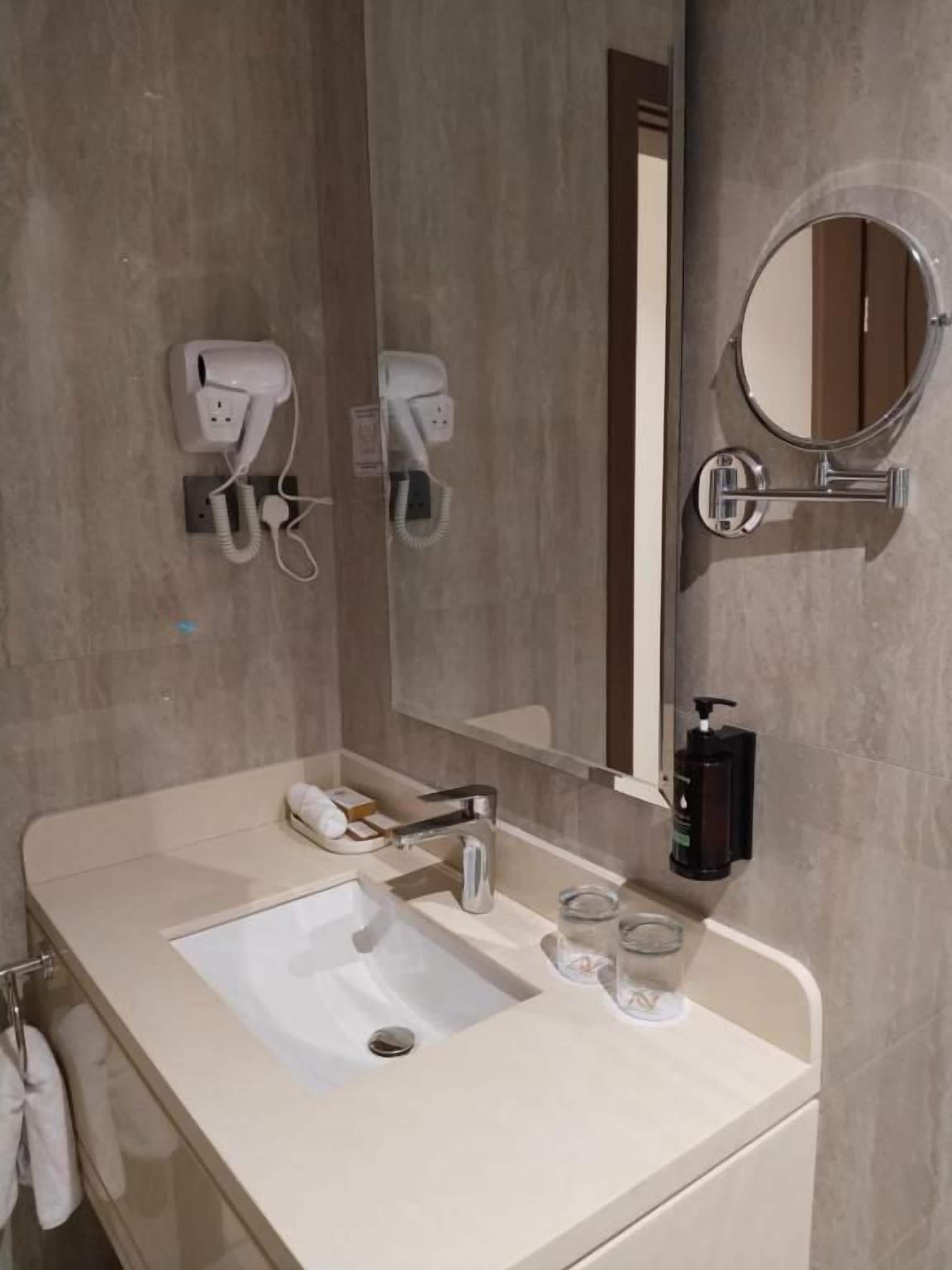 A bathroom with a sink, mirror, and two hair dryers mounted on the wall.