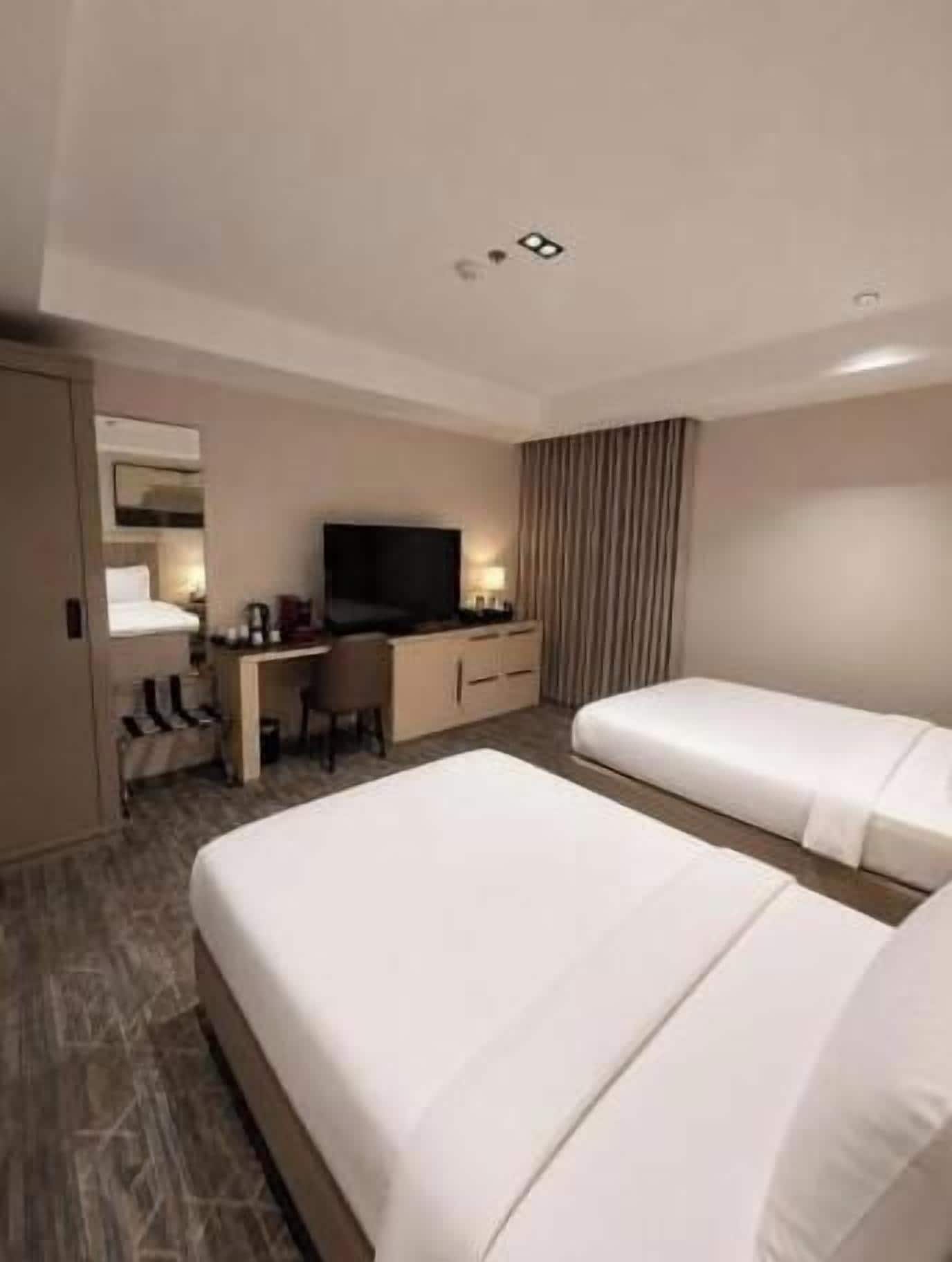 A hotel room with two beds, a desk, a television, and a mirror.