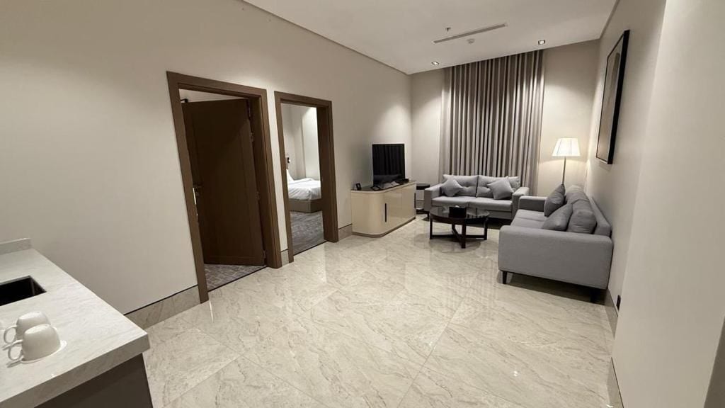 Ein modernes Hotelzimmer mit Marmorboden, einer Couch, einem Fernseher, einem Nachttisch und einer Lampe.