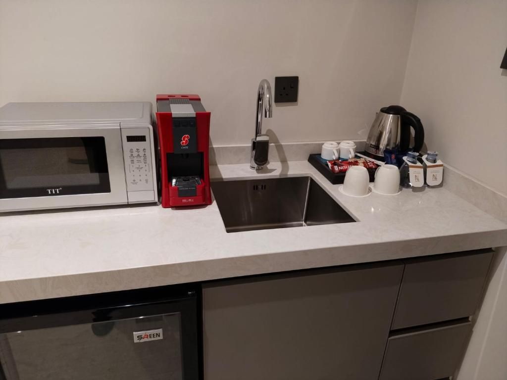 A kitchenette with a microwave, coffee maker, sink, and coffee cups.