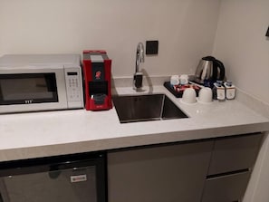 A kitchenette with a microwave, coffee maker, sink, and coffee cups. - NILVA HOTEL فندق نيلفا (Abha)