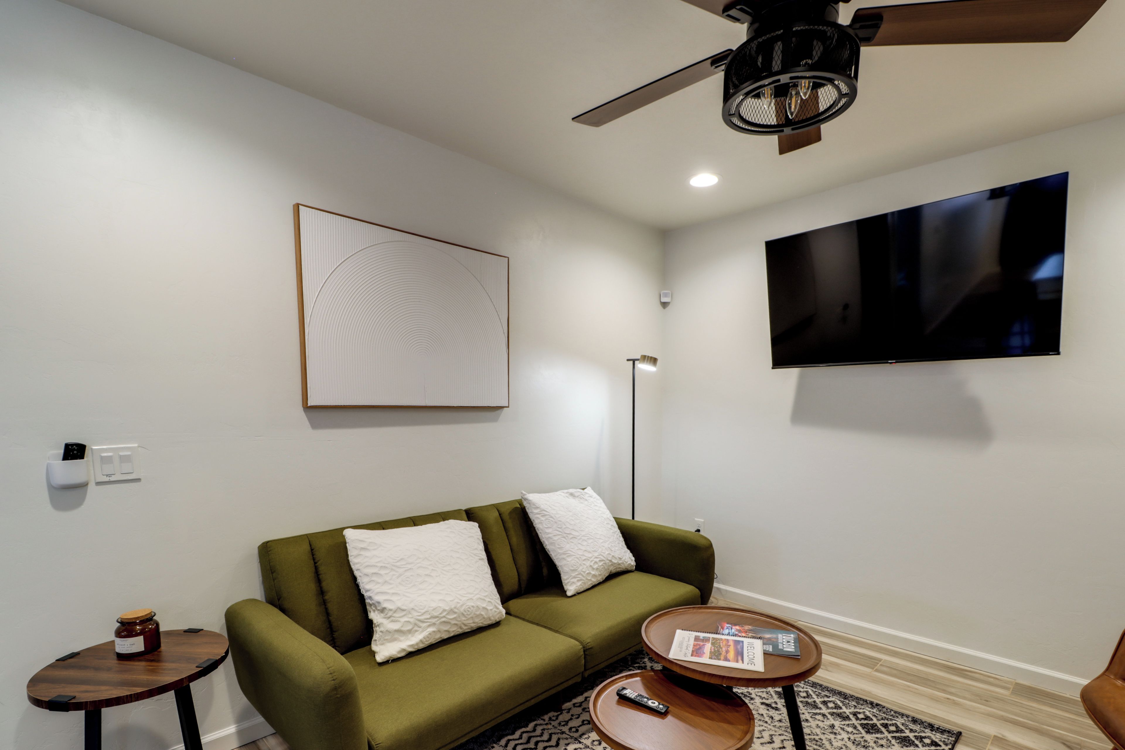 A modern living room with a green sofa, a flat-screen TV, a ceiling fan, and a small side table with a remote control.