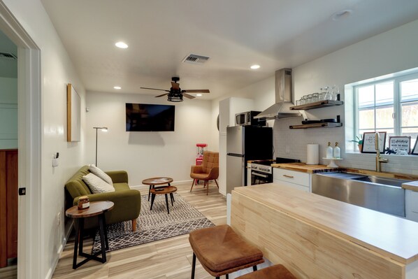 Eine moderne Küche mit Backofen, Mikrowelle und Spüle aus Edelstahl. Es gibt einen Essbereich mit Holztisch und Stühlen sowie eine Sitzecke mit Sofa und kleinem Teppich.