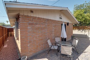 Eine Terrassenfläche mit einer Ziegelmauer, einem Tisch mit Stühlen und einem Sonnenschirm.