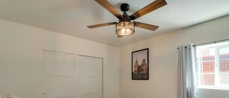 A bedroom with a bed, a ceiling fan, a window with curtains, and a door.