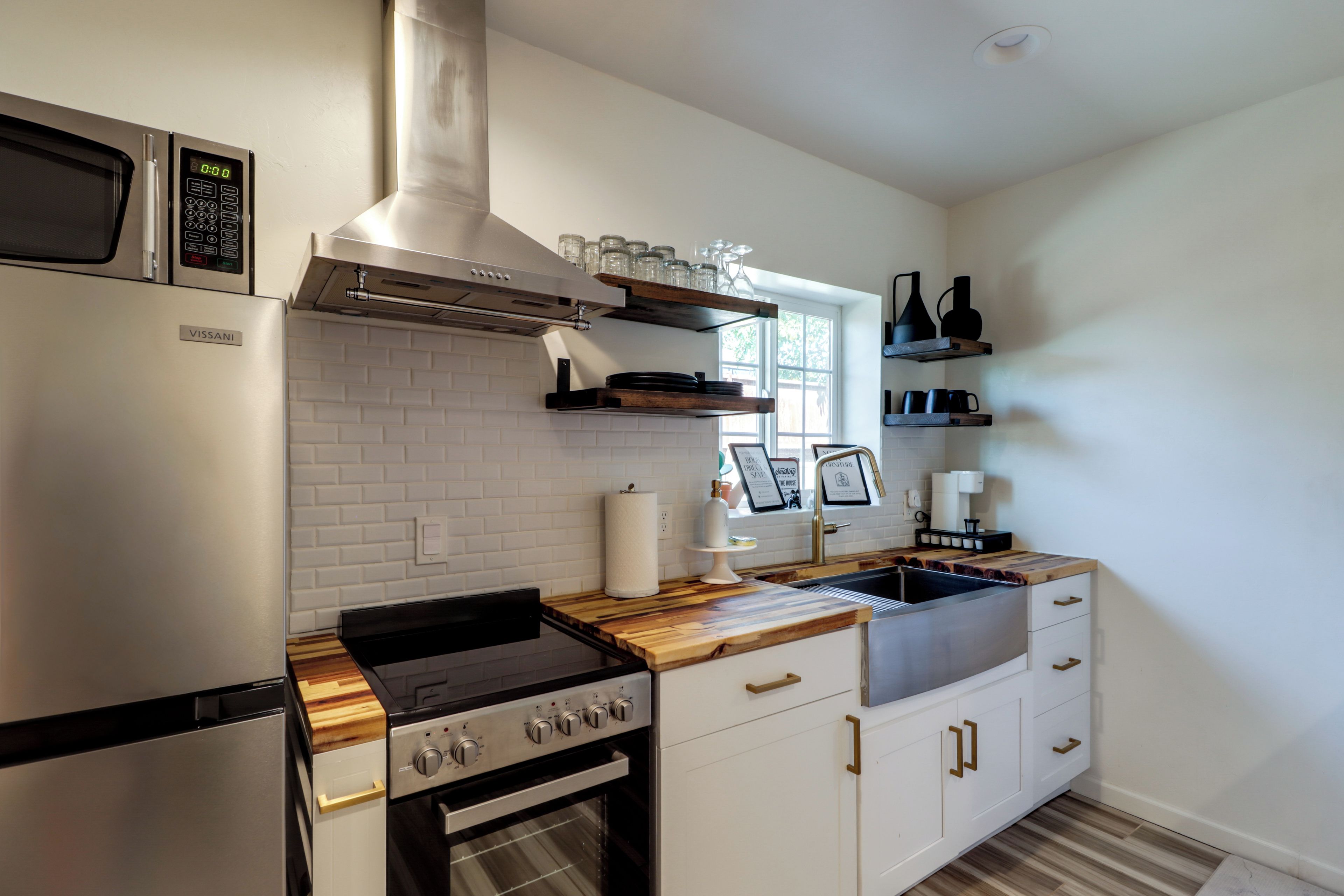 A modern kitchen with stainless steel appliances, wooden countertops, and white cabinetry.
