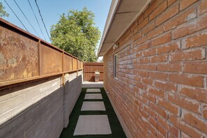 Passadís estret amb una paret de maó d'un costat i una tanca de fusta de l'altre, que condueix a una zona de fusta.