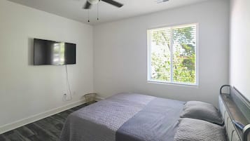 A bedroom with a bed, a ceiling fan, a TV mounted on the wall, and a window with blinds.