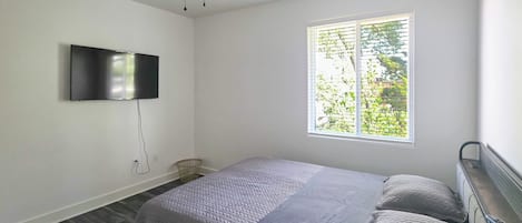 A bedroom with a bed, a ceiling fan, a TV mounted on the wall, and a window with blinds.