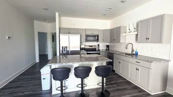 A modern kitchen with a central island, bar stools, and a microwave.