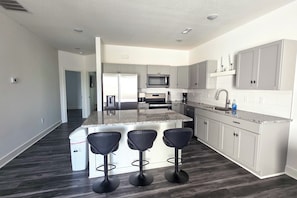 A modern kitchen with a central island, bar stools, and a microwave.