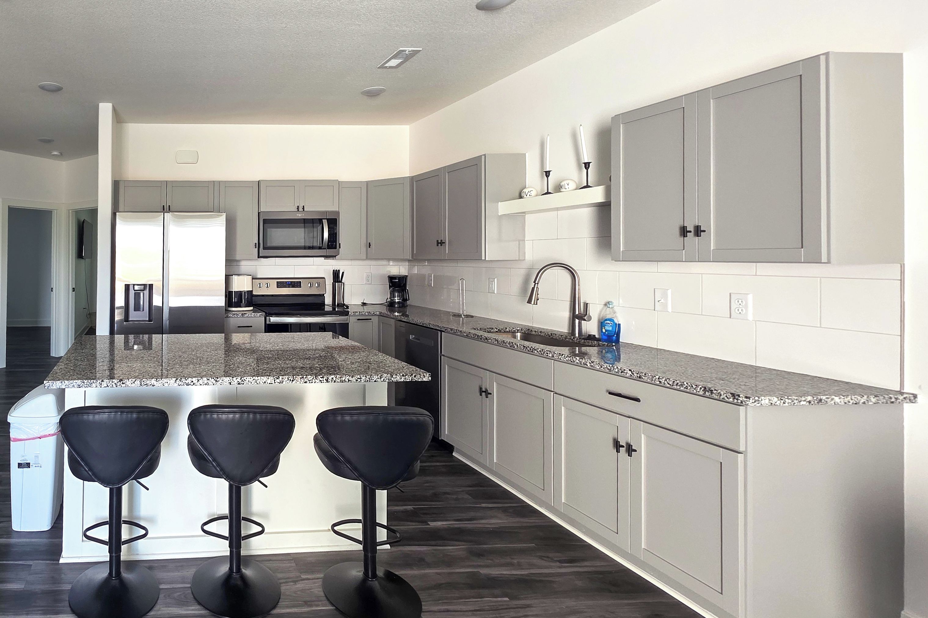 A modern kitchen with a central island, bar stools, and a microwave.
