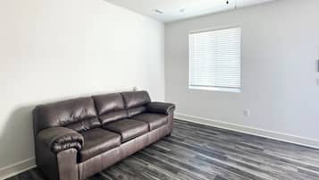 A room with a dark brown leather sofa, a window with blinds, and a ceiling fan.