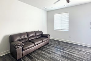 A room with a dark brown leather sofa, a window with blinds, and a ceiling fan.