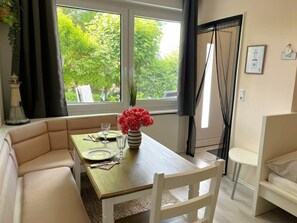 Ein Essbereich mit einem Tisch für zwei Personen, einer Blumenvase und Blick auf Grünfläche.