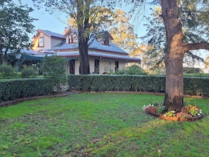 Une maison avec un jardin, un grand arbre et une haie.