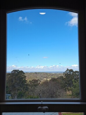 Une vue à travers une fenêtre, avec un ciel dégagé, des arbres et un paysage lointain.