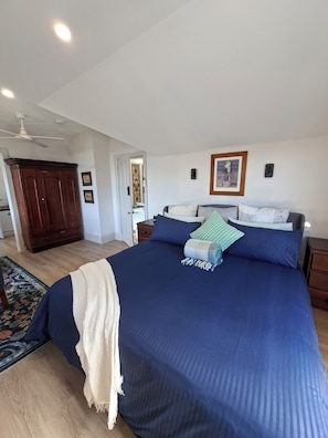 Un dormitorio con una cama grande, un ventilador de techo, un armario y una puerta que da a otra habitación.