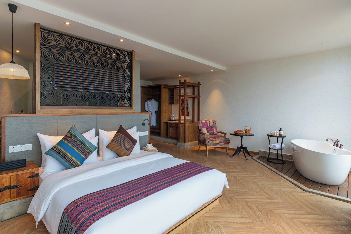 Habitación de hotel con una cama grande, un área de descanso con una silla, una bañera y un panel decorativo en la pared.
