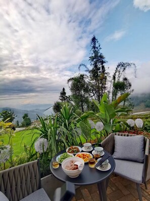 Un área de comedor al aire libre con una mesa preparada para una comida, rodeada de exuberante follaje y una vista panorámica.