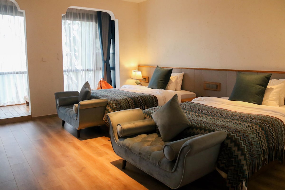 Habitación de hotel con dos camas, un sofá, una silla y un ventanal con cortinas.