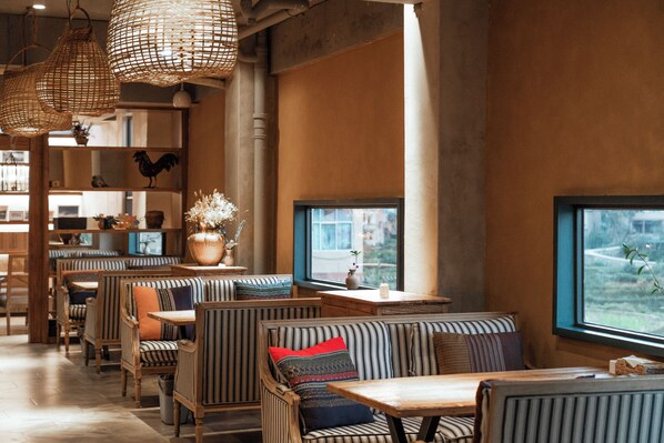 A restaurant interior with wooden furniture, hanging wicker lamps, and a view through the window.