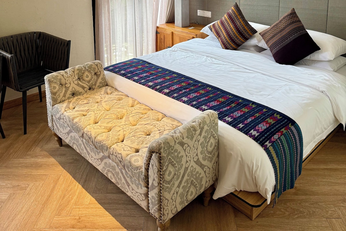 Una habitación de hotel con una cama, un sofá, una silla, una mesita de noche y una lámpara.