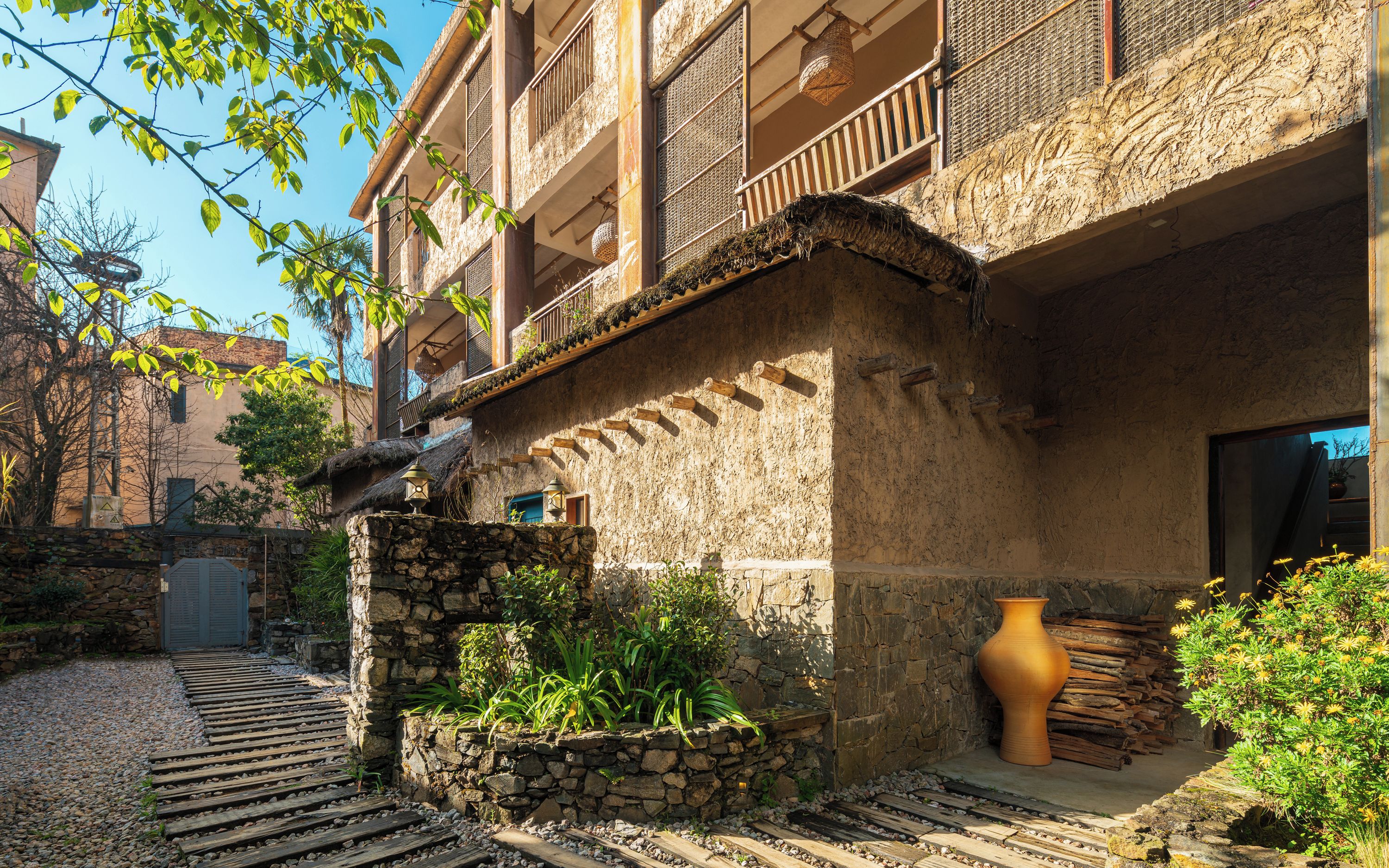 Un patio con un muro de piedra, un jarrón grande y un banco de madera.