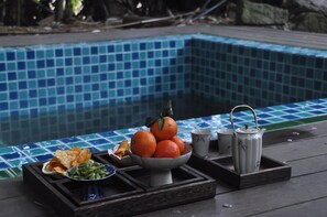 A poolside table with a bowl of oranges, a bowl of snacks, and a teapot.