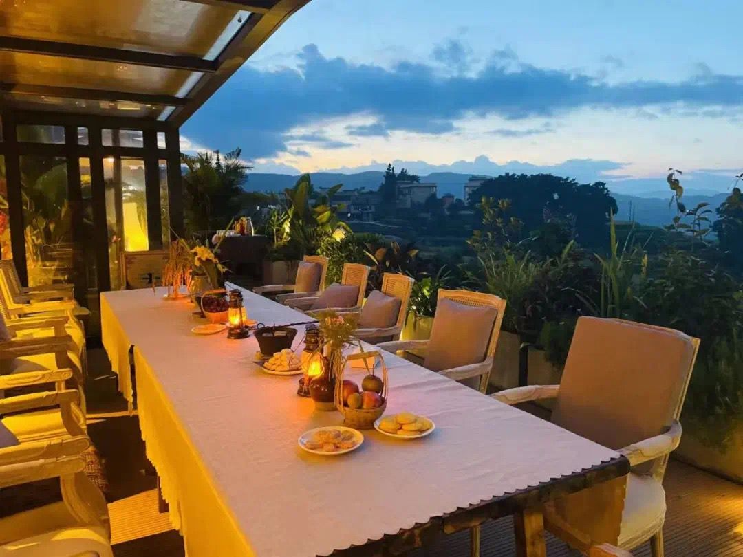 Un área de comedor al aire libre con una mesa preparada para dos, rodeada de sillas, con vista a un paisaje montañoso.