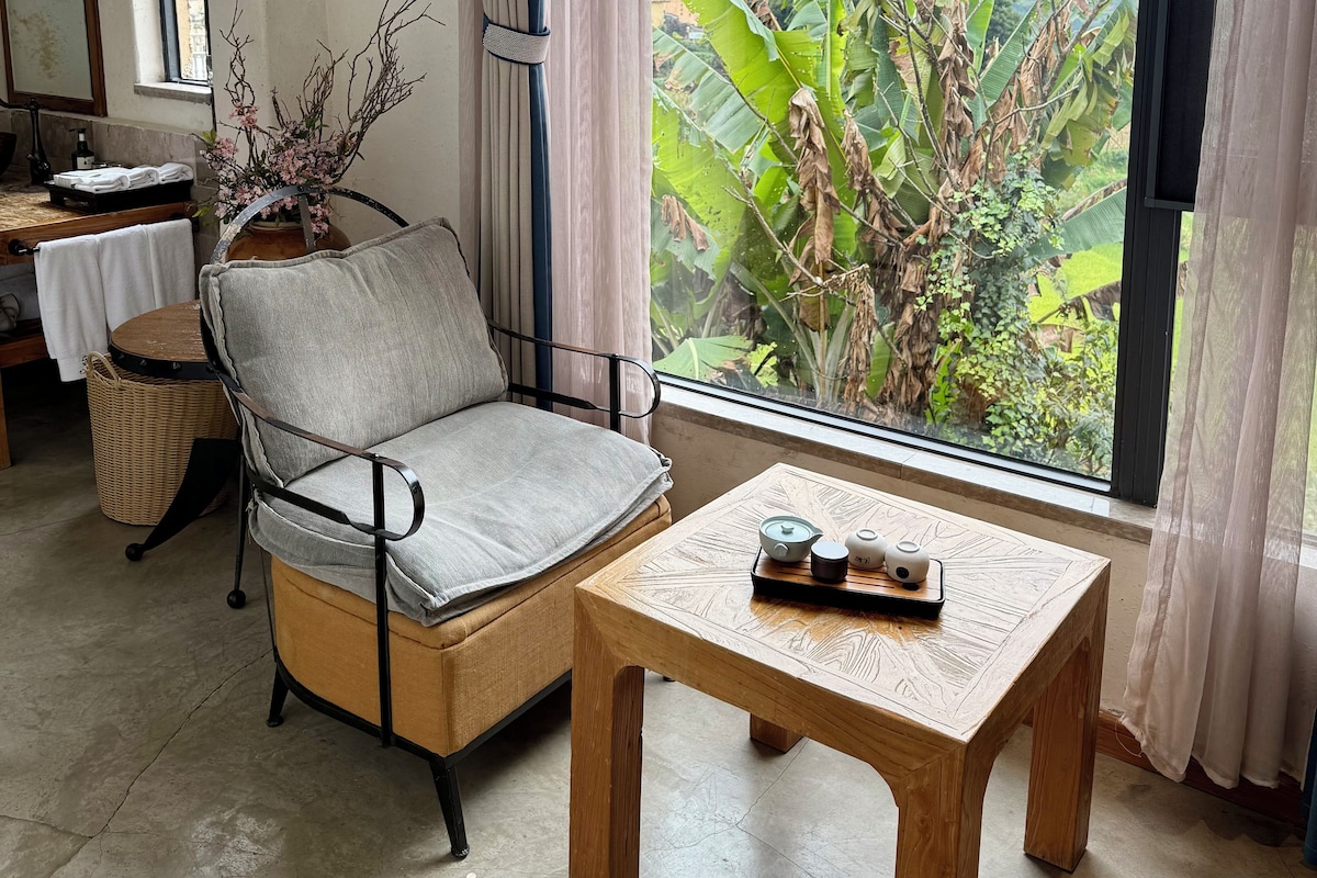 Una habitación con sofá, una mesa de madera con bandeja, una cesta de mimbre y vistas a zonas verdes por la ventana.