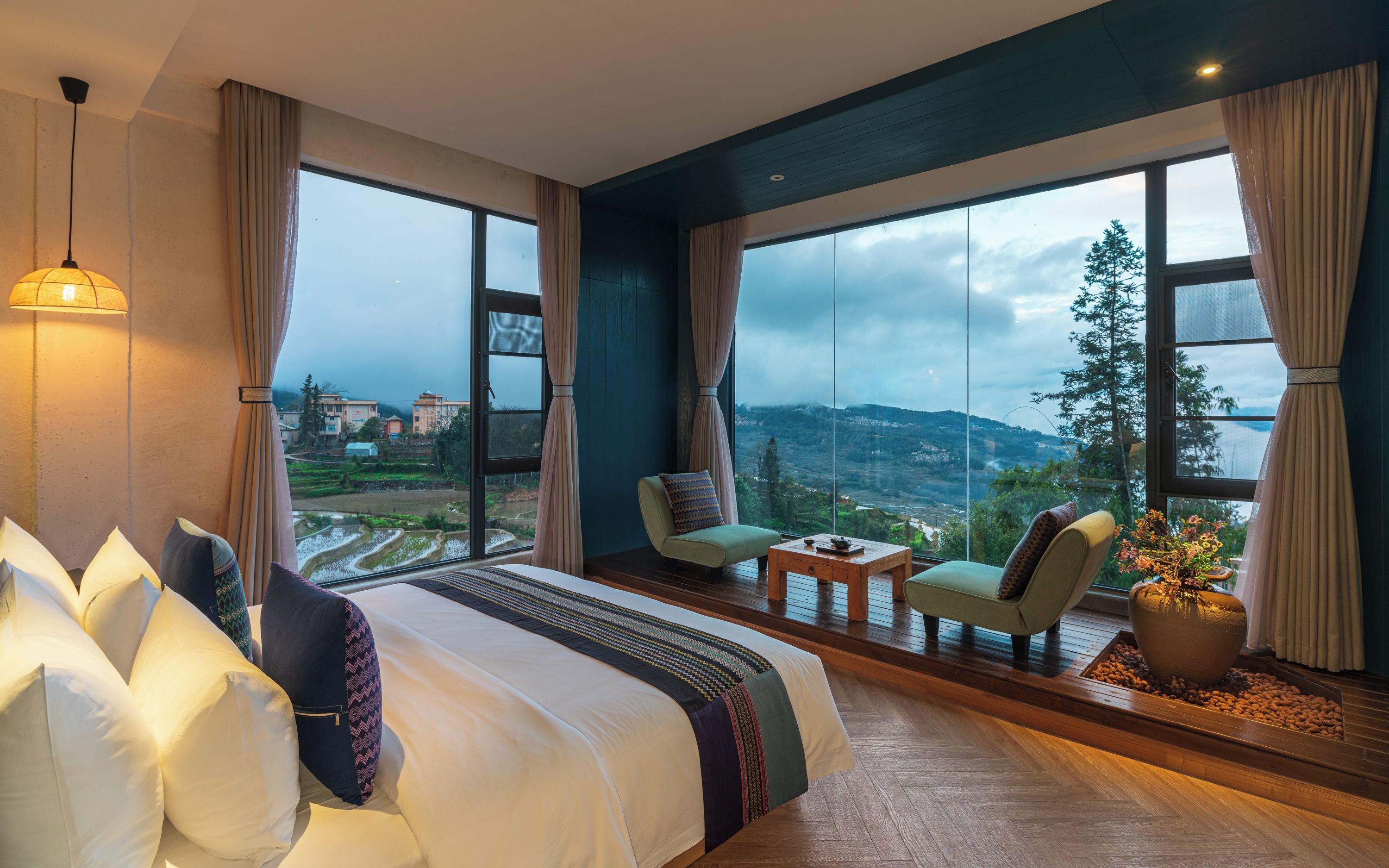 Habitación de hotel con una cama grande, dos sillones, una mesita y vistas a un paisaje montañoso.