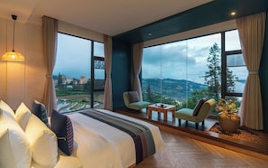 Habitación de hotel con una cama grande, dos sillones, una mesita y vistas a un paisaje montañoso.
