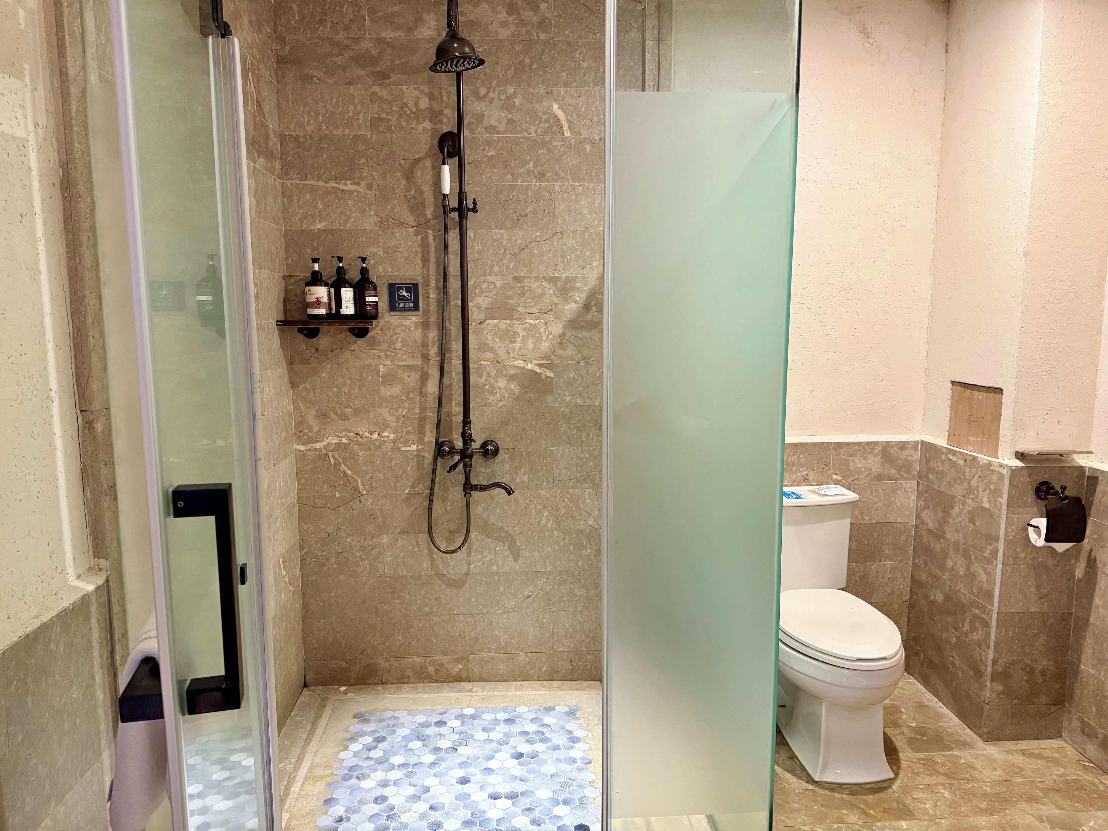 A bathroom with a glass-enclosed shower, a toilet, and a tiled floor.