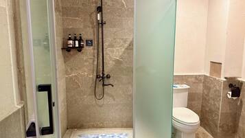A bathroom with a glass-enclosed shower, a toilet, and a tiled floor.