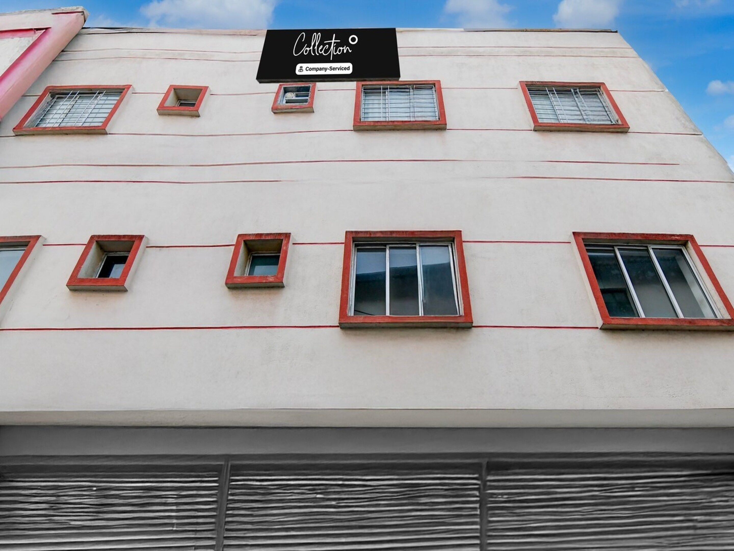 Fachada de edificio con varias ventanas, algunas con marcos rojos, y un letrero que indica que ofrece servicios de empresa.