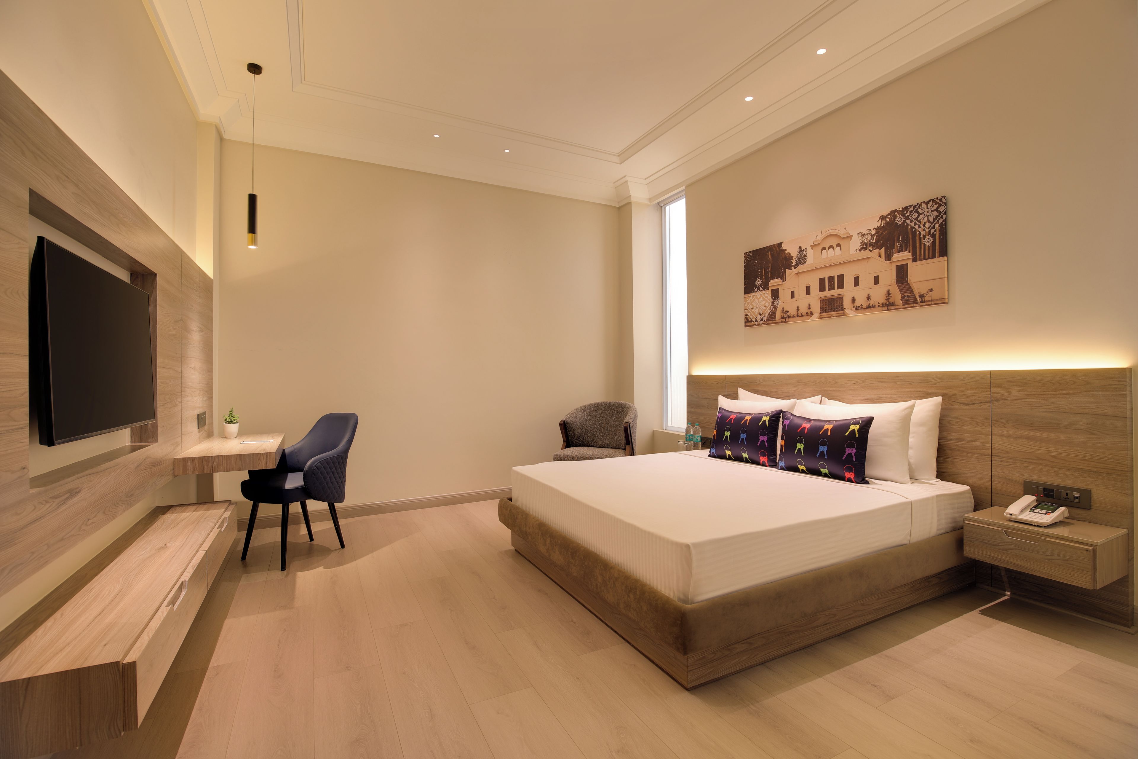 A modern hotel room with a large bed, a desk, a chair, a flat-screen TV, and a nightstand with a phone.