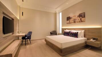 A modern hotel room with a large bed, a desk, a chair, a flat-screen TV, and a nightstand with a phone.